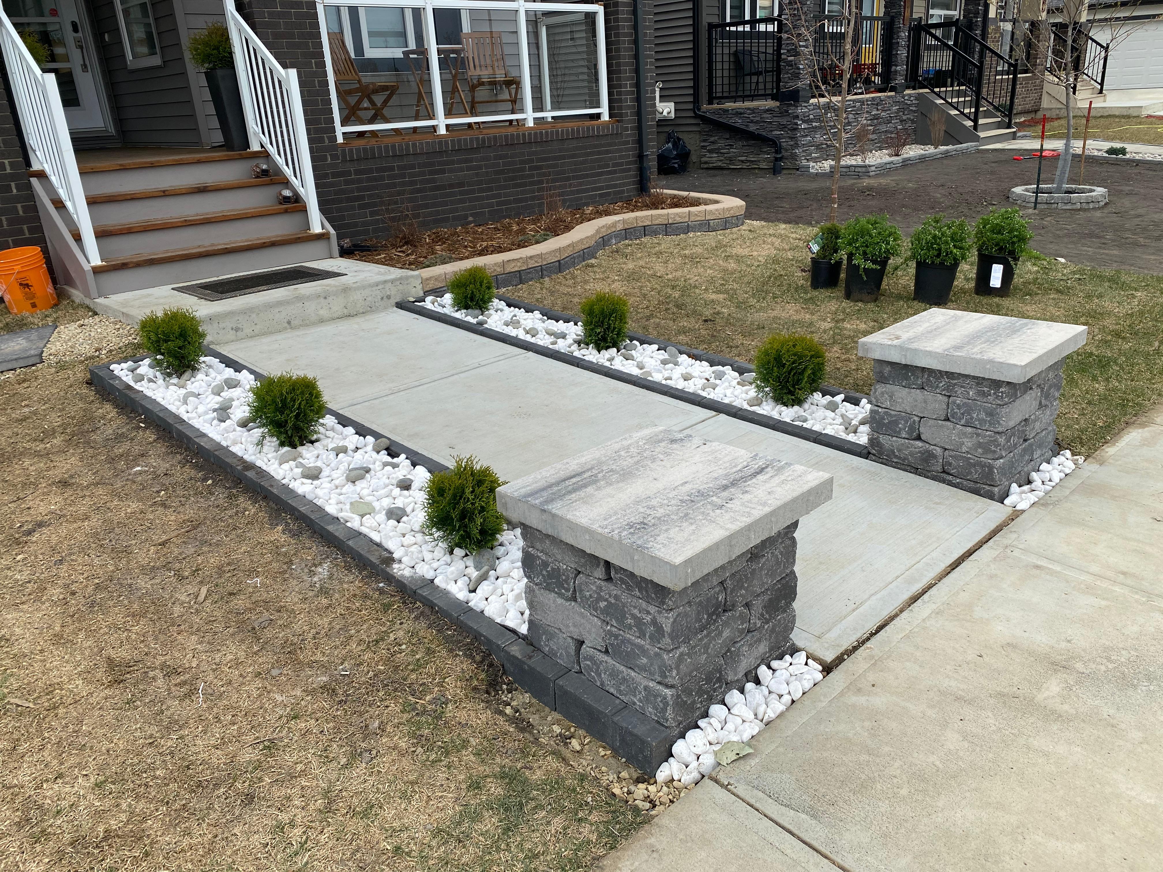 Front yard with stacked stone pillars and concrete walkway lined with globe cedars